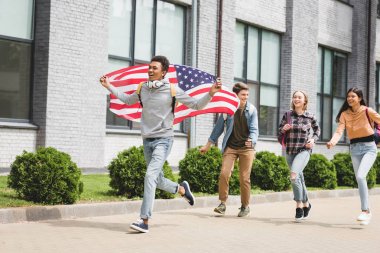 mutlu gençler gülümseyerek, Amerikan bayrağı tutarak ve dışında çalışan