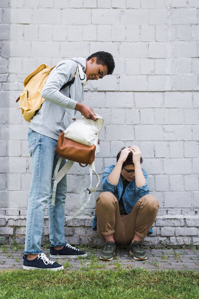 african american boy holding backpack of frightened boy in glasses 