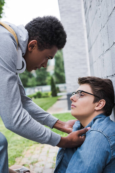 aggressive and brunette african american boy bulling frightened boy in glasses 