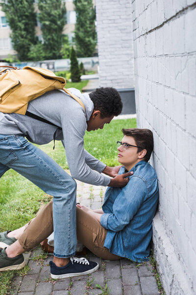 aggressive and brunette african american boy bulling frightened boy in glasses 