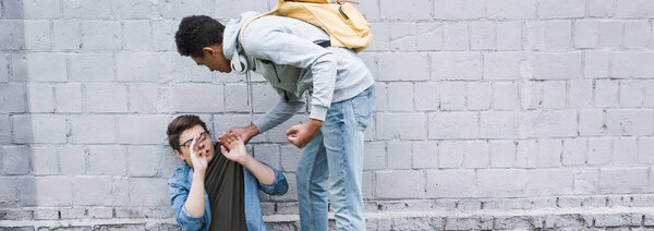 panoramic shot of aggressive and brunette african american boy bulling frightened boy in glasses 
