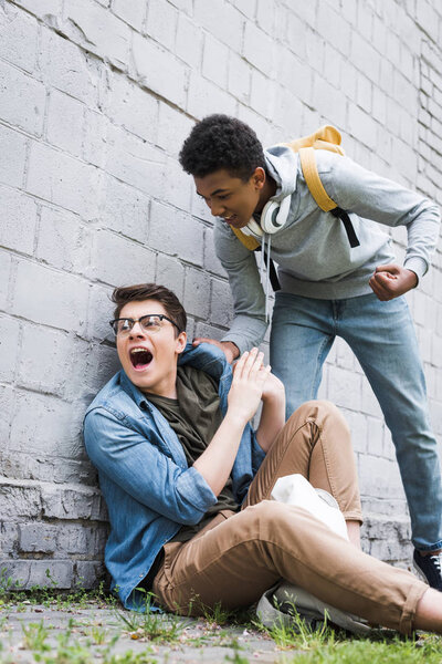 aggressive and brunette african american boy going to punch frightened boy in glasses 