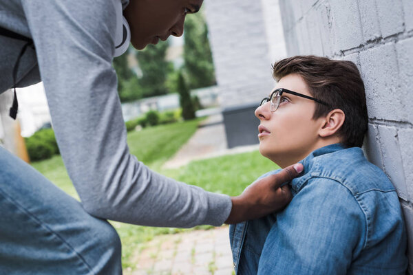 aggressive and brunette african american boy bulling scared boy in glasses 