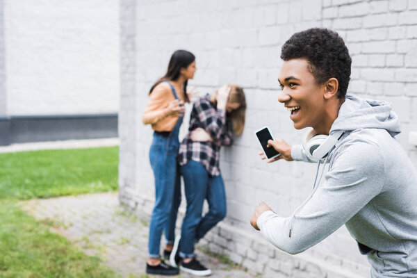 selective focus of smiling african american boy shooting bulling of scared teenager