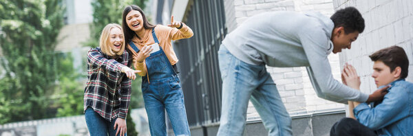 panoramic shot of african american boy in hoodie and jeans bulling boy and teenager shooting it and pointing with fingers 