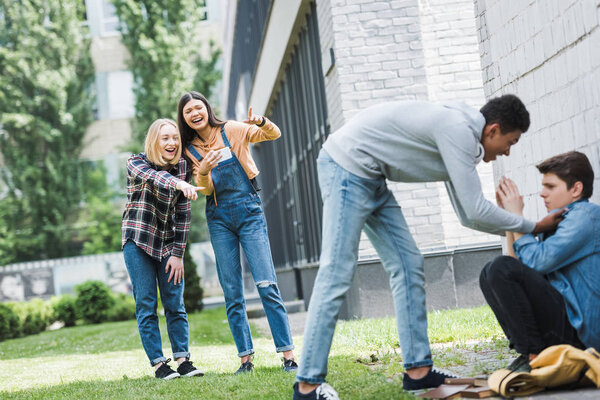 african american boy in hoodie and jeans bulling boy and teenager shooting it and pointing with fingers 