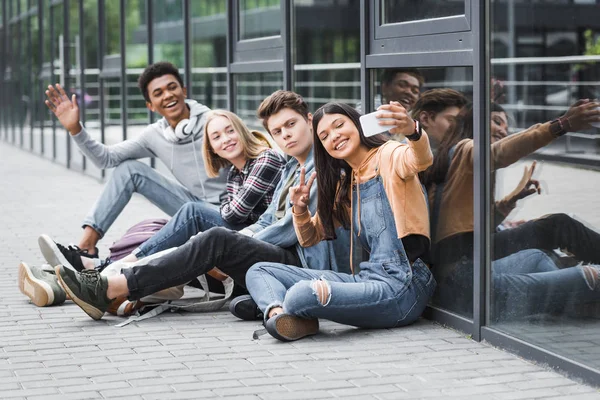 mutlu arkadaşlar gülümseyerek, otururken ve akıllı telefon ile selfie çekmek 