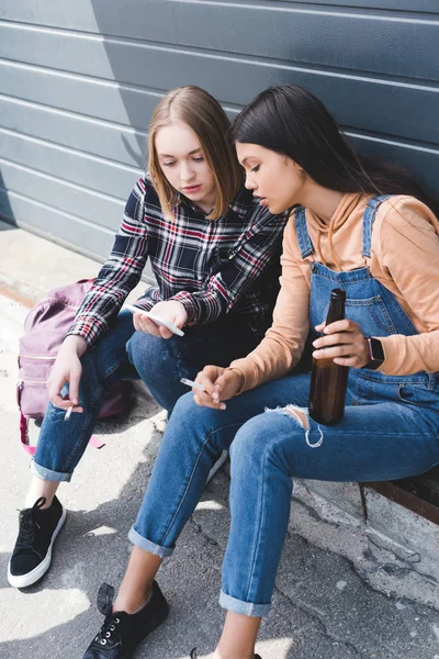 Graziosi Amici Fumare Sigarette Tenendo Birra Seduto Guardando Smartphone — Foto Stock