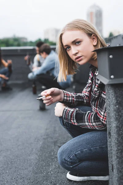 selective focus of blonde and pretty teenager smoking cigarette and looking away