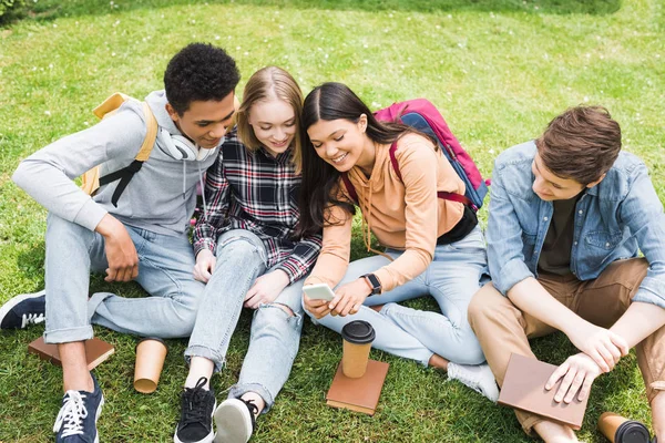 Adolescentes Sonrientes Felices Sentados Hierba Mirando Teléfono Inteligente — Foto de Stock