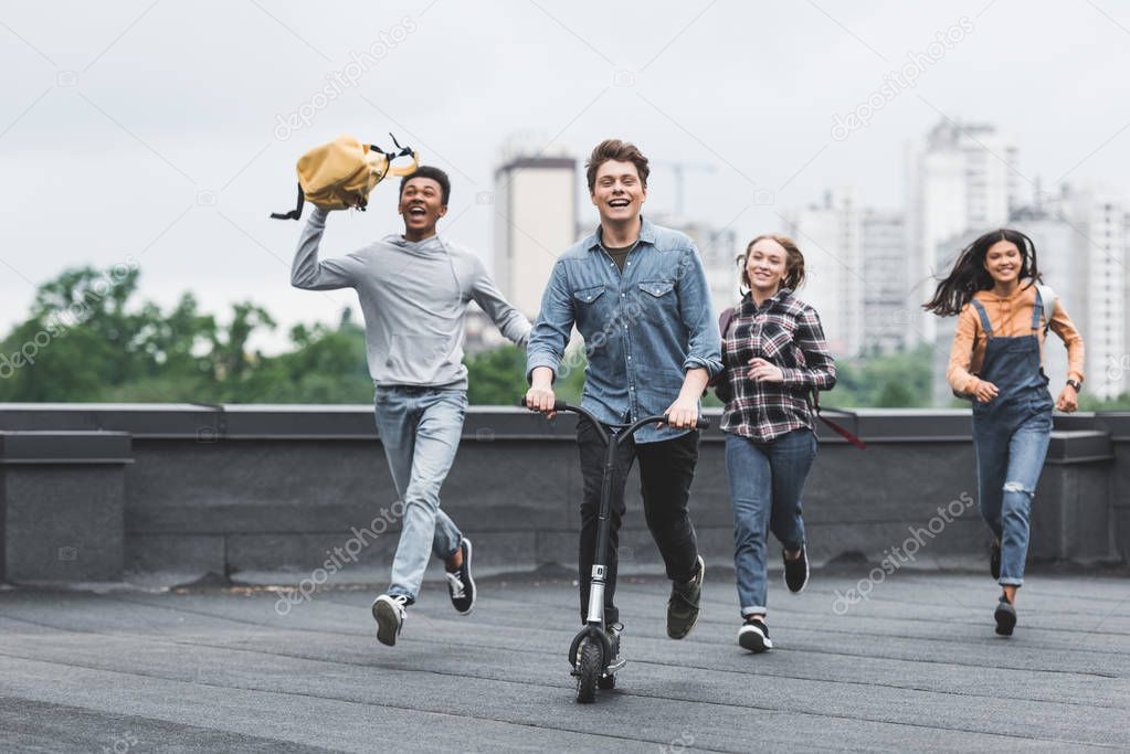 playful and smiling teenagers running on roof and riding scooter 