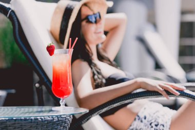 arka planda güneşlenme güzel gülümseyen esmer genç kadın ile masada çilek ile serin kokteyl seçici odak