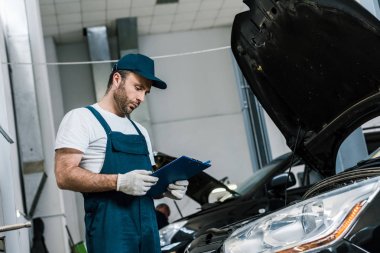 arabanın yanında kalem ve pano tutan kap yakışıklı sakallı tamirci