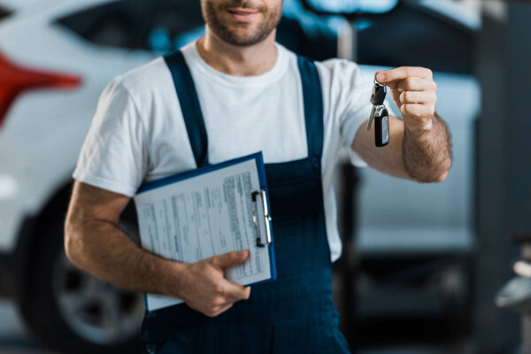 cropped view of car mechanic holding clipboard and key 