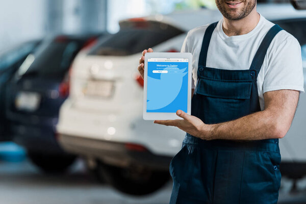 KYIV, UKRAINE - JUNE 7, 2019: cropped view of cheerful car mechanic holding digital tablet with twitter app on screen in car service 