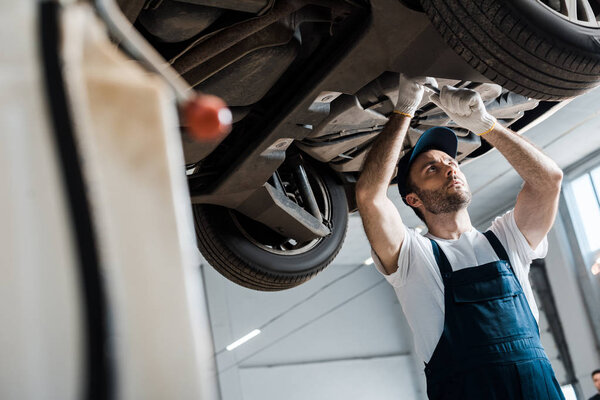 selective focus of bearded car mechanic repairing automobile in car service 
