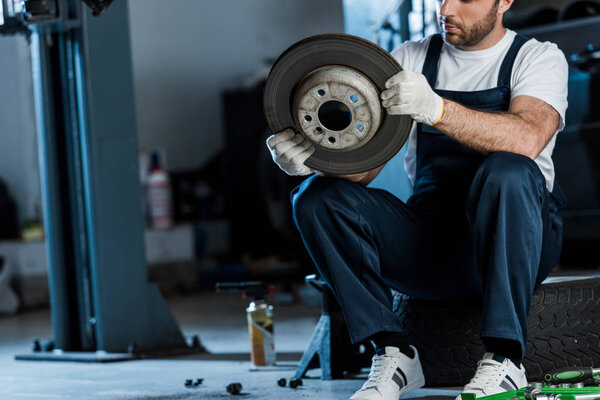 обрезанный вид автомеханика, держащего металлический автомобильный тормоз, сидящего на автомобильной шине
 