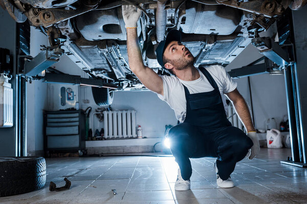 handsome auto mechanic in cap repairing automobile in car service 