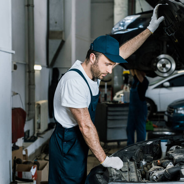 handsome bearded car mechanic in gloves looking at car engine 