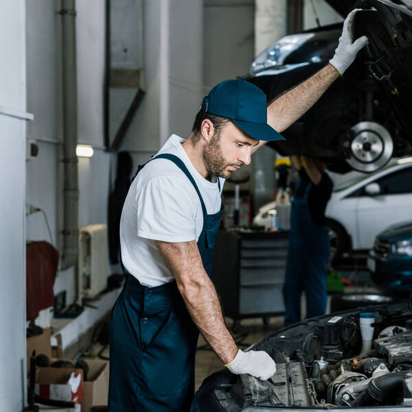 handsome bearded car mechanic in gloves looking at car engine 