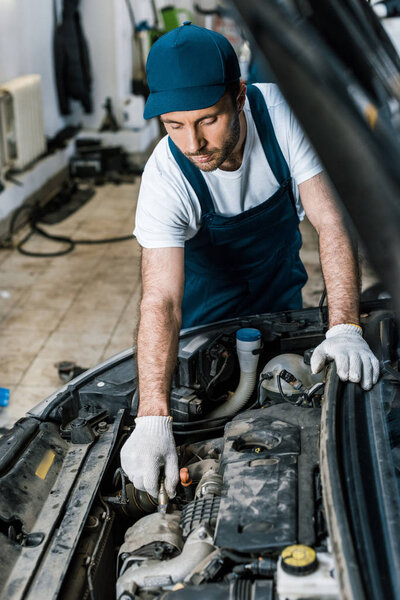 selective focus of handsome car mechanic fixing auto in car service 