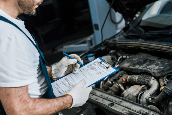 cropped view of bearded repairman holding pen and clipboard near car
