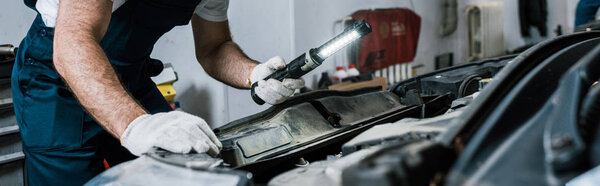 panoramic shot of auto mechanic holding flashlight near car 
