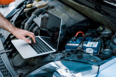 cropped view of car mechanic using laptop with blank screen near car  clipart