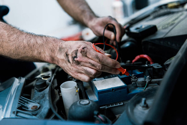 cropped view auto mechanic with mud on hands fixing automobile in car repair station 