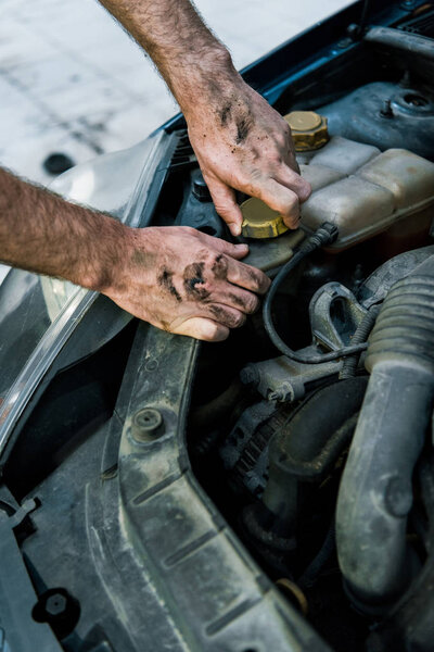 cropped view of car mechanic with mud on hands changing car oil 