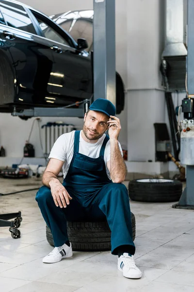 Cheerful Bearded Man Touching Cap Sitting Car Tire — Stock Photo, Image