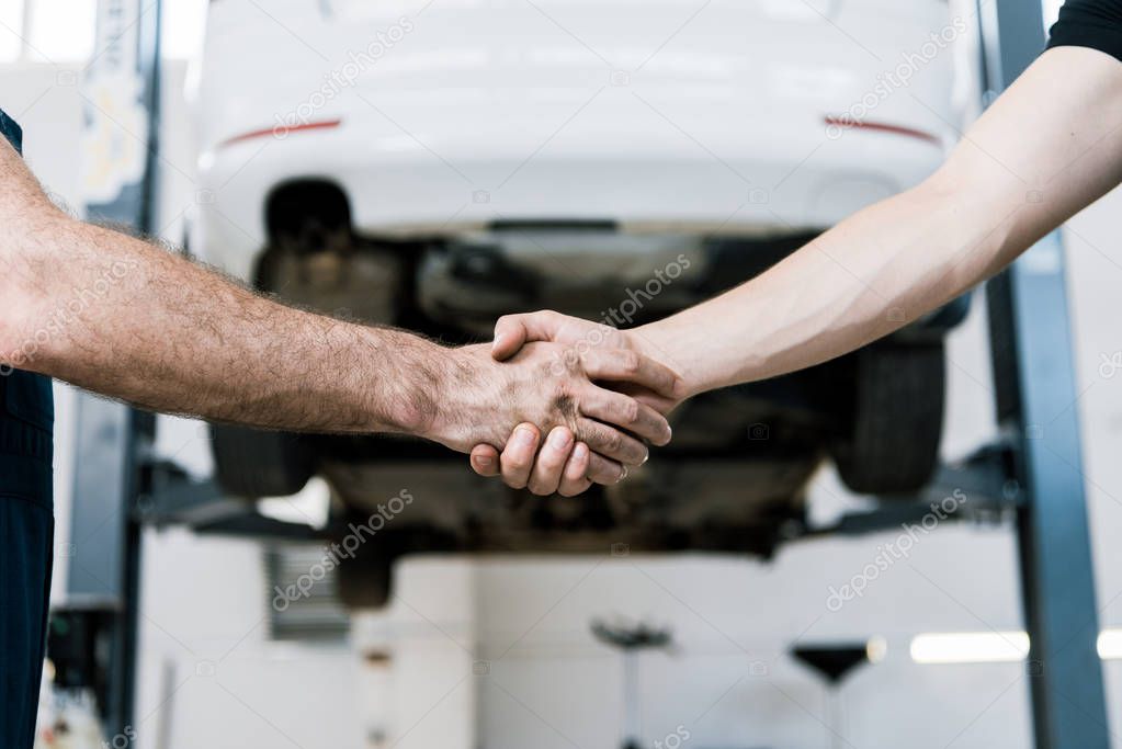 cropped view of car mechanic shaking hands with man in garage 