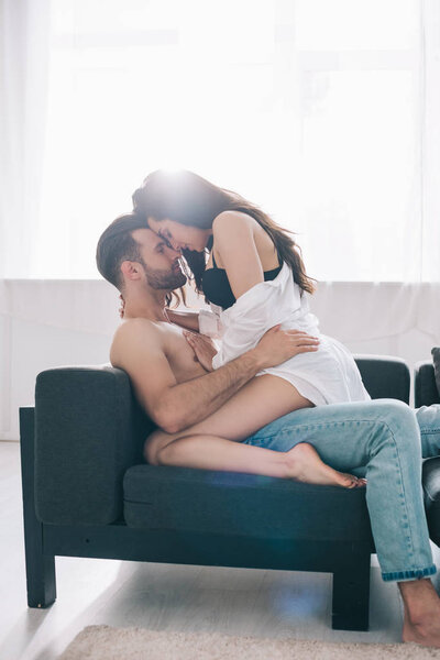 shirtless and handsome man hugging with brunette woman in bra on sofa 