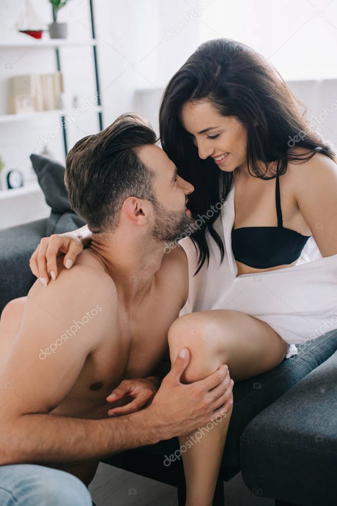 attractive and smiling woman in shirt and bra hugging with shirtless man 