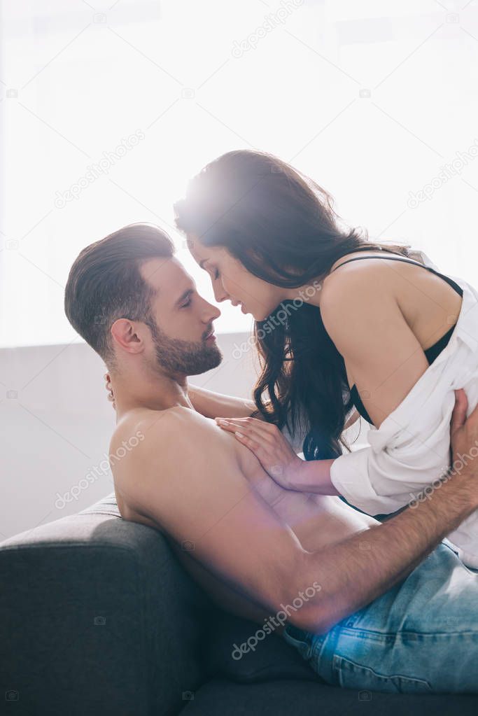 side view of shirtless and handsome man kissing and hugging with brunette woman 