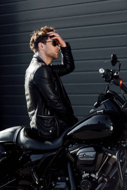handsome young man sitting on motorcycle and readjusting hair  clipart