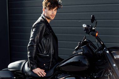 handsome young man in leather jacket sitting on black motorcycle  clipart