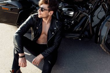 siyah motosiklet yakınında yerde oturan gömleksiz genç adam