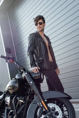  deri ceket ve çıplak gövde siyah motosiklet yakınında duran güneş gözlüğü genç adam