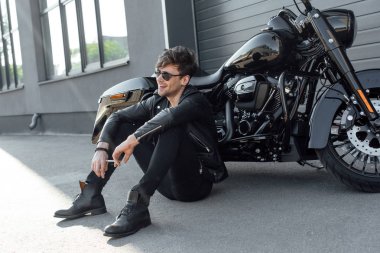 young man sitting near black motorcycle and holding cigarette clipart