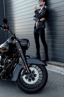 motosiklet yakın duvara yakın duran ve sigara tutan güneş gözlüğü ve deri ceket motosiklet tam uzunlukta görünümü 