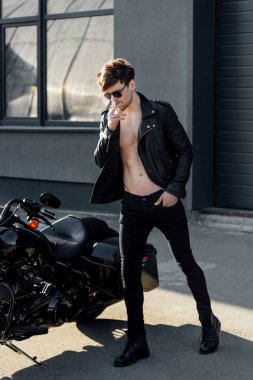çıplak gövde sigara ve motosiklet yakınında yürüyüş ile yakışıklı genç motosikletçi tam uzunlukta görünümü