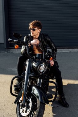 genç adam güneş ışığında motosiklet üzerinde oturan ve uzağa bakıyor 
