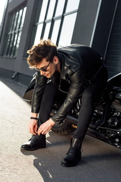 黒いオートバイに座っている間にブーツをひもで縛る若い男 — ストック写真