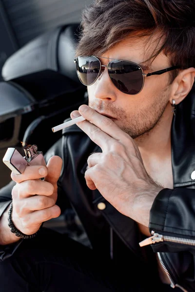黒い新しいオートバイの近くに座っている間 サングラスでタバコを点灯する若者の肖像写真 — ストック写真