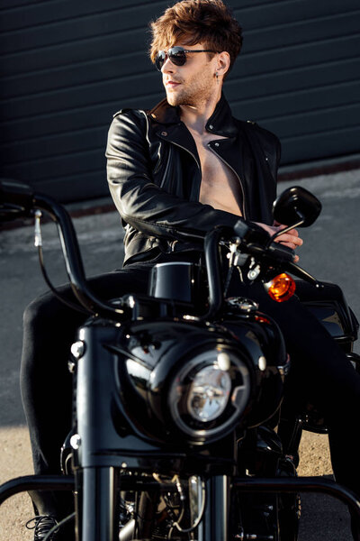 shirtless handsome young man in leather jacket resting on black motorcycle