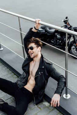 çıplak gövde ile genç adam yerde oturan, gülerek ve metal çit tutan 