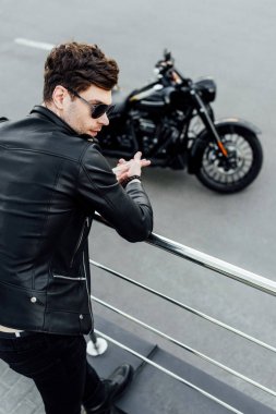 arka planda motosiklet ile metal çit yanında duran deri ceket adam seçici odak