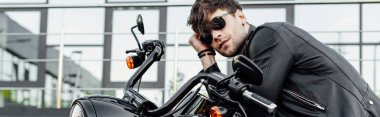 panoramic shot of handsome young man in leather jacket resting while sitting on motorcycle  clipart