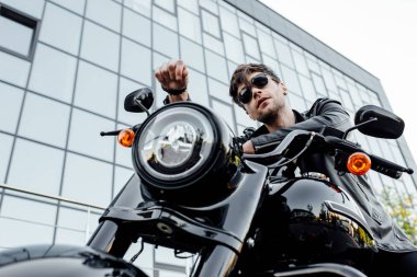 motosiklet üzerinde otururken uzağa bakarak güneş gözlüğü yakışıklı genç motosikletçi düşük açı görünümü